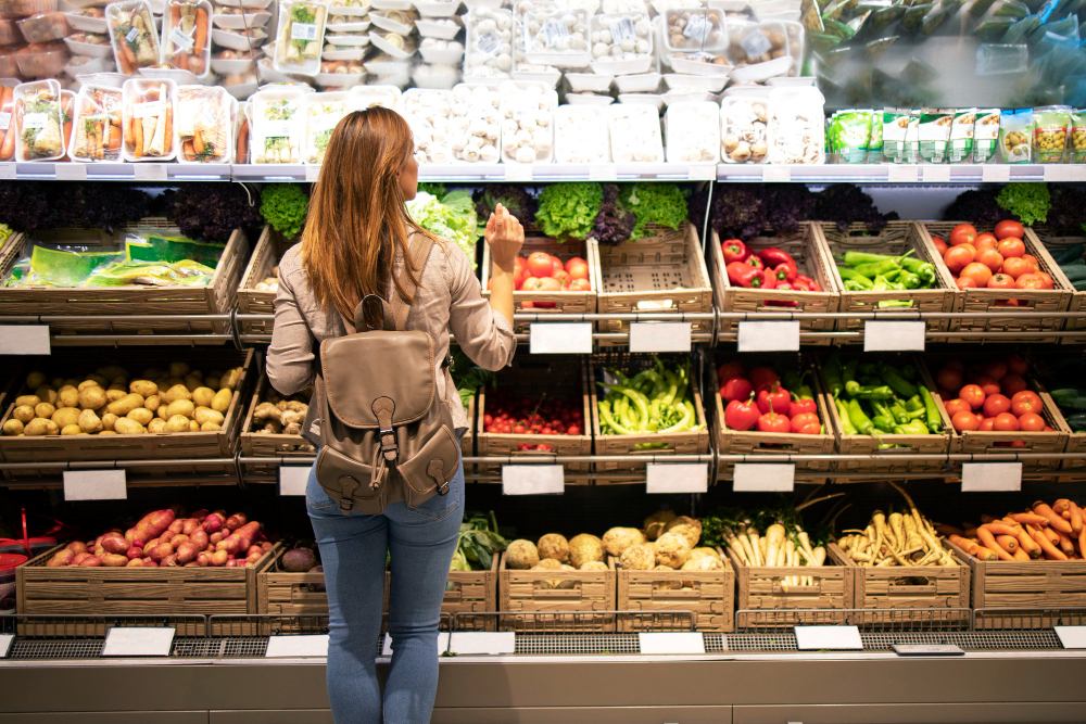 Une femme debout devant des étagères de légumes, choisissant ce qu'elle va acheter.