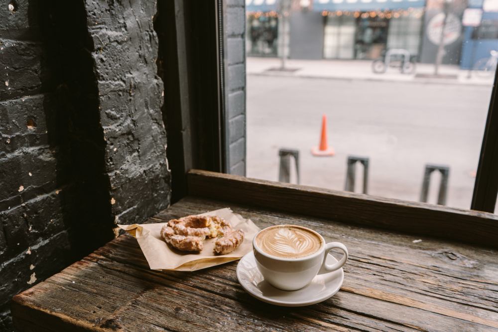 Tasse de café à côté d'un biscuit posé sur le rebord de la fenêtre