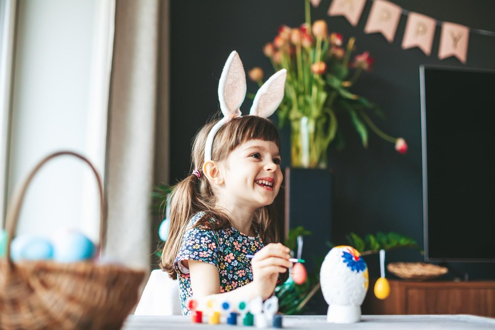 Petite fille rieuse avec des oreilles de lapin peignant un œuf de Pâques